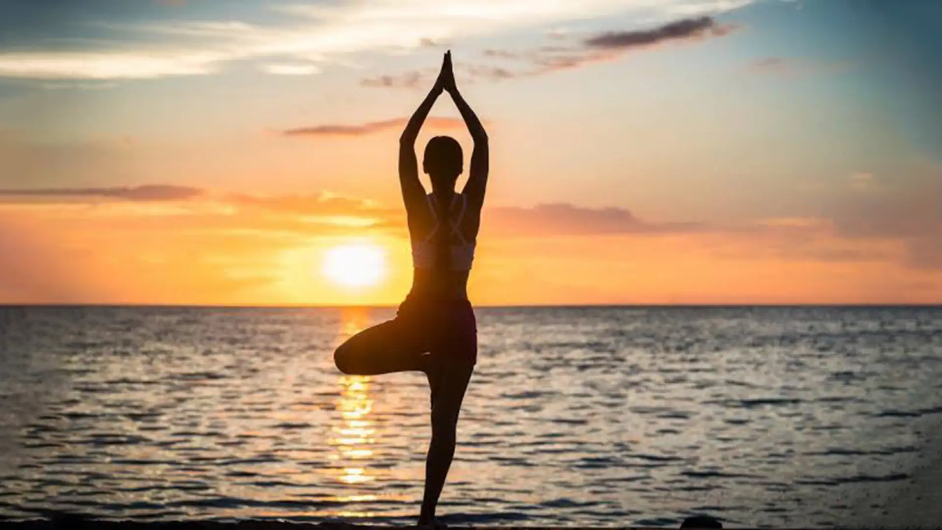 Person practicing yoga in tree pose on the beach at sunset over the ocean